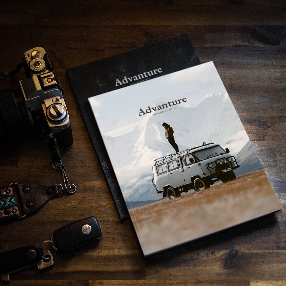 Two issues of Advanture Magazine on a coffee table beside a vintage film camera, capturing the spirit of vanlife and slow journalism.