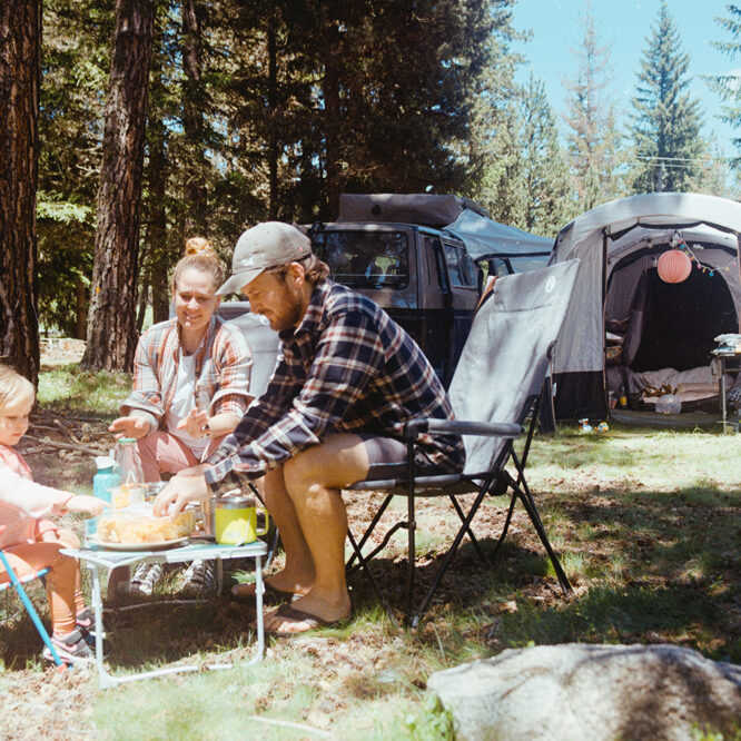 Family sitting on camping chairs under £100 near a campervan in a UK forest campsite