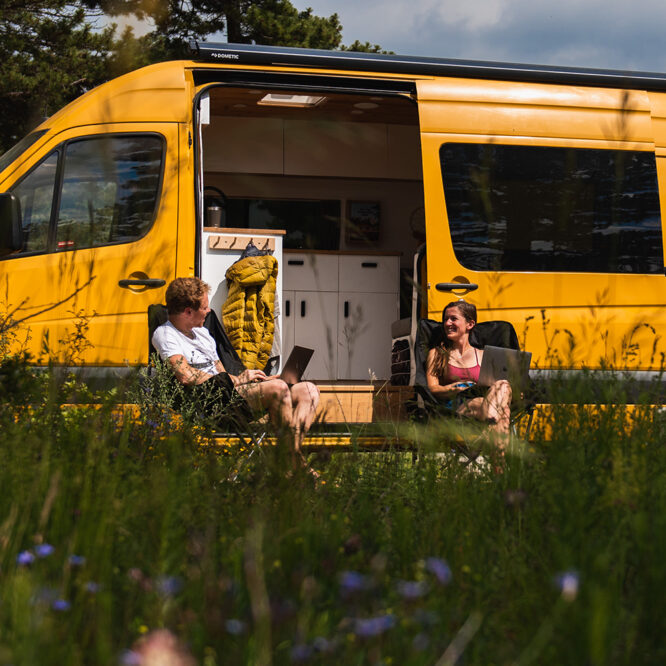 Charlie and Dale sitting in front of their yellow campervan, Ringo, smiling at the camera for the Nohma van conversion interview